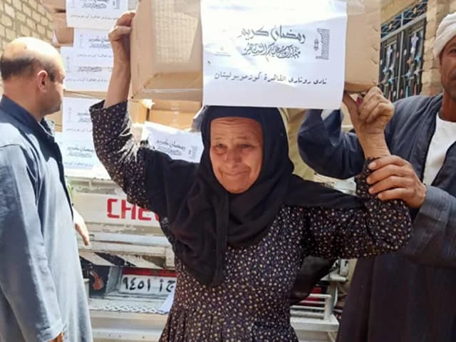 A woman carrying a Ramadan food package on her head, the box labelled in Arabic with the club’s name